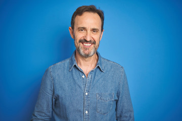Handsome middle age senior man with grey hair over isolated blue background with a happy and cool smile on face. Lucky person.