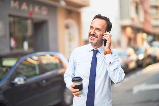 Middle age handsome businessman talking on the smartphone drinking take away coffee smiling