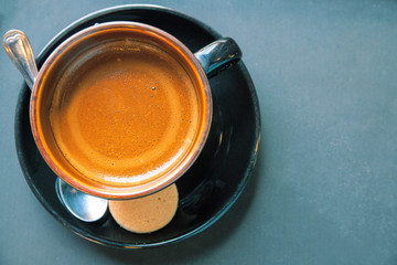 Cappuccino coffee in black ceramic cup on grey table, top view photo. Morning coffee mug with cookie.