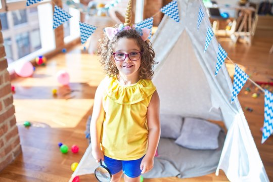 Beautiful toddler wearing glasses and unicorn diadem standing and smiling at kindergarten