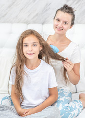 Happy young mother is combing her daughter at home