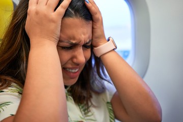 Fototapeta premium Young traveller woman sitting inside plane at the airport with sky view from the window feeling sick, headache and nauseas