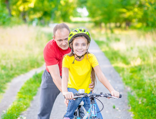 Dad teaches his daughter to ride a bicycle in the summer park