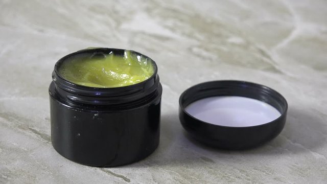 Finger dipping into a jar of CBD salve slow motion