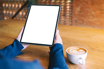 Mockup image of a woman holding black tablet pc with blank white screen with coffee cup on wooden table