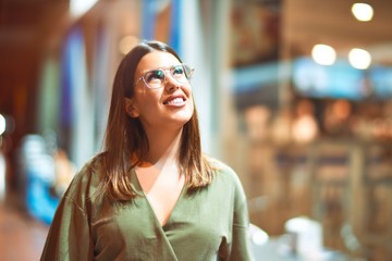 Young beautiful girl smiling happy and confident walking at the town street, standing with a smile on face around night lights bokeh