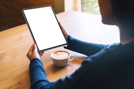 Mockup image of a woman holding black tablet pc with blank white screen with coffee cup on wooden table