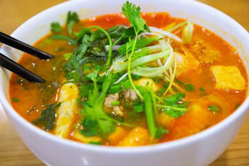 Pho soup with meat broth, vegetables and greenery in white ceramic bowl with sticks. Traditional vietnamese cuisine