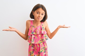 Young beautiful child girl wearing pink floral dress standing over isolated white background clueless and confused expression with arms and hands raised. Doubt concept.