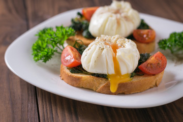 The yolk flowing from the poached egg on a piece of bread in a white plate on a wooden table.