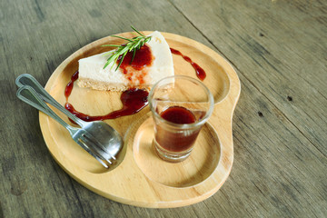 Cheesecake pie slice topped with strawberry syrup with spoon and fork on a wooden plate, Sweet food with brown table in background