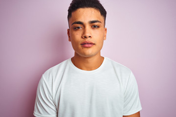 Young brazilian man wearing t-shirt standing over isolated pink background with a confident expression on smart face thinking serious