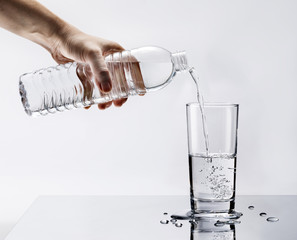 Hand pouring fresh pure water from bottle into a glass on the table with water drops, Healthcare...