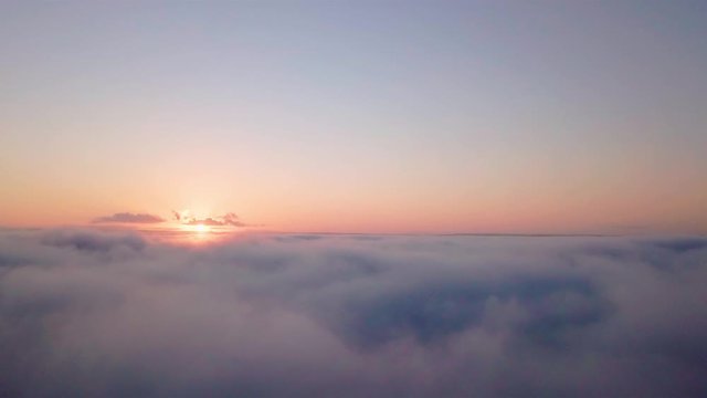 Aerial dreamy and scenic view at sunrise low above the clouds. Forward camera motion close to the surface of clouds with sun on the left side with slow and relaxing forward motion.
