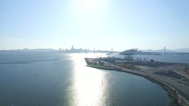 High altitude pan to the right over San Francisco and bay. To the right are shipping cranes and large steel shipping crates. Daytime. 4k H.265