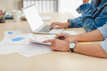 close up hand asian creative designer team casual meeting and brainstorming on desk with paperwork and online data on laptop in meeting room at modern office.business planning concept