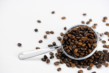 Roasted  coffee seeds in metal colander on white background.