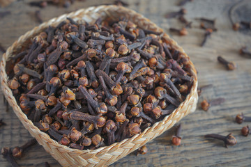 dried cloves on hand made bamboo wood bowl and wooden background.