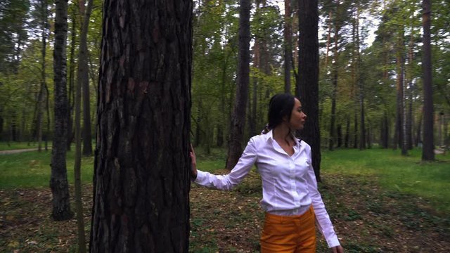 A beautiful girl from Russia walks alone in the forest. She has a very deep look and is wearing a white shirt. Autumn weather. Slow motion.