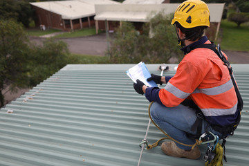 Rope access inspector technician holding looking at the paper work while inspecting fall arrest,...