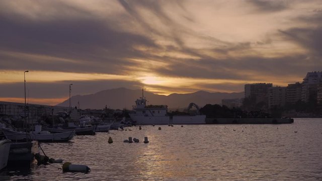 Marbella fishing port at sunset, fishing boats bobbing up and down in the harbor (text in video is a registration number of a boat and a for sale sign)