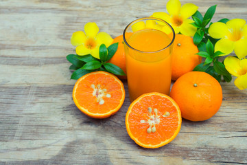 Orange juice in glass with slice oranges decorated with yellow flowers and green leafs on wooden