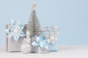 Graceful home decor for christmas celebration - pastel blue and metallic gift boxes with silver christmas tree, shiny ball on white wood board, copy space.