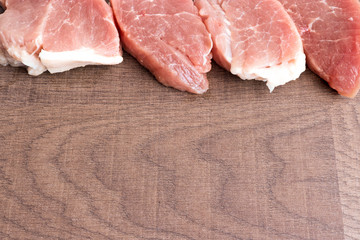 Large slices of pork on an old wooden surface. The concept of cholesterol food. Raw meat before cooking. Copy space.