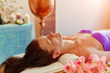 ayurveda massage alternative healing therapy.beautiful caucasian female getting shirodhara treatment lying on a wooden table in India salon.
