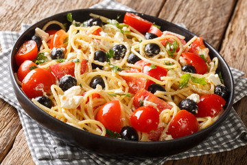 Traditional Greek pasta spaghetti salad with cheese, olives, tomatoes close-up on a plate on the table. horizontal