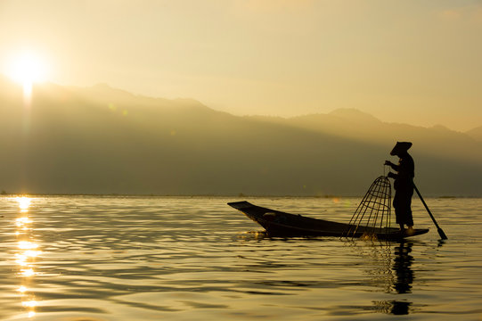 The silhouette of a fisherman on a boat in the morning at Inle Lake is a fresh water lake In the mountainous area of Shan State in Myanmar.