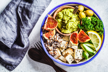Buddha bowl with quinoa, tofu, kale, fig and guacamole hummus in a white plate, top view.