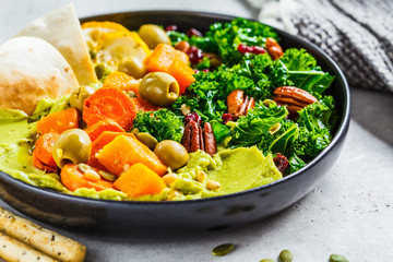 Avocado hummus with baked vegetables, olives, nuts and berries in black plate. Healthy vegan food concept.