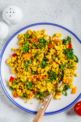 Tofu scramble with vegetables in a white plate, top view. Vegan Alternative fried eggs.