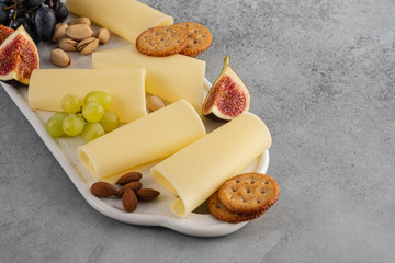 Cheese slices on white board with honey, figs, olives, grapes.