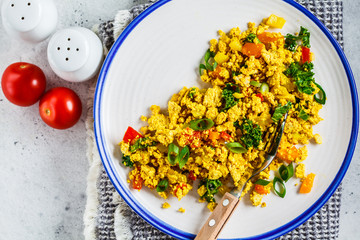 Tofu scramble with vegetables in a white plate, top view. Vegan Alternative fried eggs.