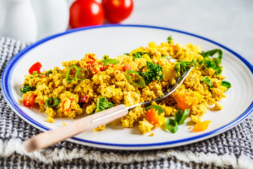Tofu scramble with vegetables in a white plate. Vegan Alternative fried eggs.