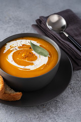 Pumpkin soup with cream on grey stone background. Copy space.
