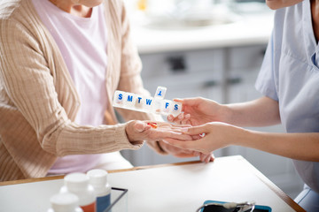 Caregiver putting pills on palm of retired woman