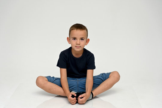 A full-length portrait of a cute boy child sitting on the floor on a white background with Vitiligo disease is a violation of the color of the skin at the initial stage. Black T-shirt, blue jeans.