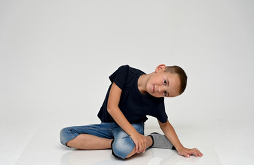 Fototapeta premium A full-length portrait of a cute boy child sitting on the floor on a white background with Vitiligo disease is a violation of the color of the skin at the initial stage. Black T-shirt, blue jeans.