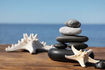 Fototapeta na wymiar Stack of stones and starfishes on wooden pier near sea, space for text Zen concept