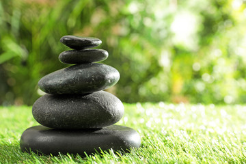 Stack of stones on green grass against blurred background, space for text. Zen concept
