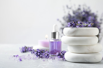 Spa stones, natural cosmetic oil and lavender flowers on grey table, space for text