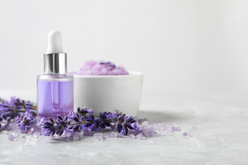 Obraz na płótnie Canvas Natural cosmetic oil, bath salt, scrub and lavender flowers on grey marble table, space for text