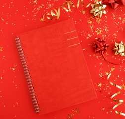 christmas or new year frame decorations in gold colors on red color background  and notebook with empty copy space for text. Xmas, holiday and celebration concept for postcard or invitation. top view 