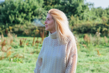 Beautiful blond woman staying and smocking cigarette in a green field