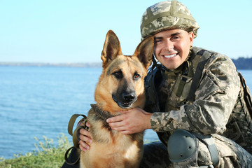 Man in military uniform with German shepherd dog near river