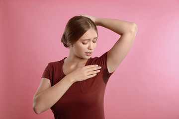 Young woman with sweat stain on her clothes against pink background. Using deodorant - obrazy, fototapety, plakaty