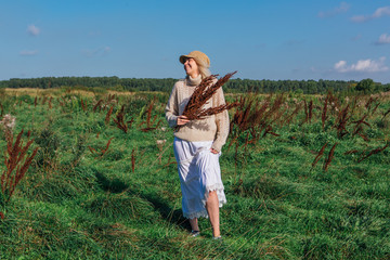 Happy beautiful blond woman walking in a green field with a bouquete of dry brown plants